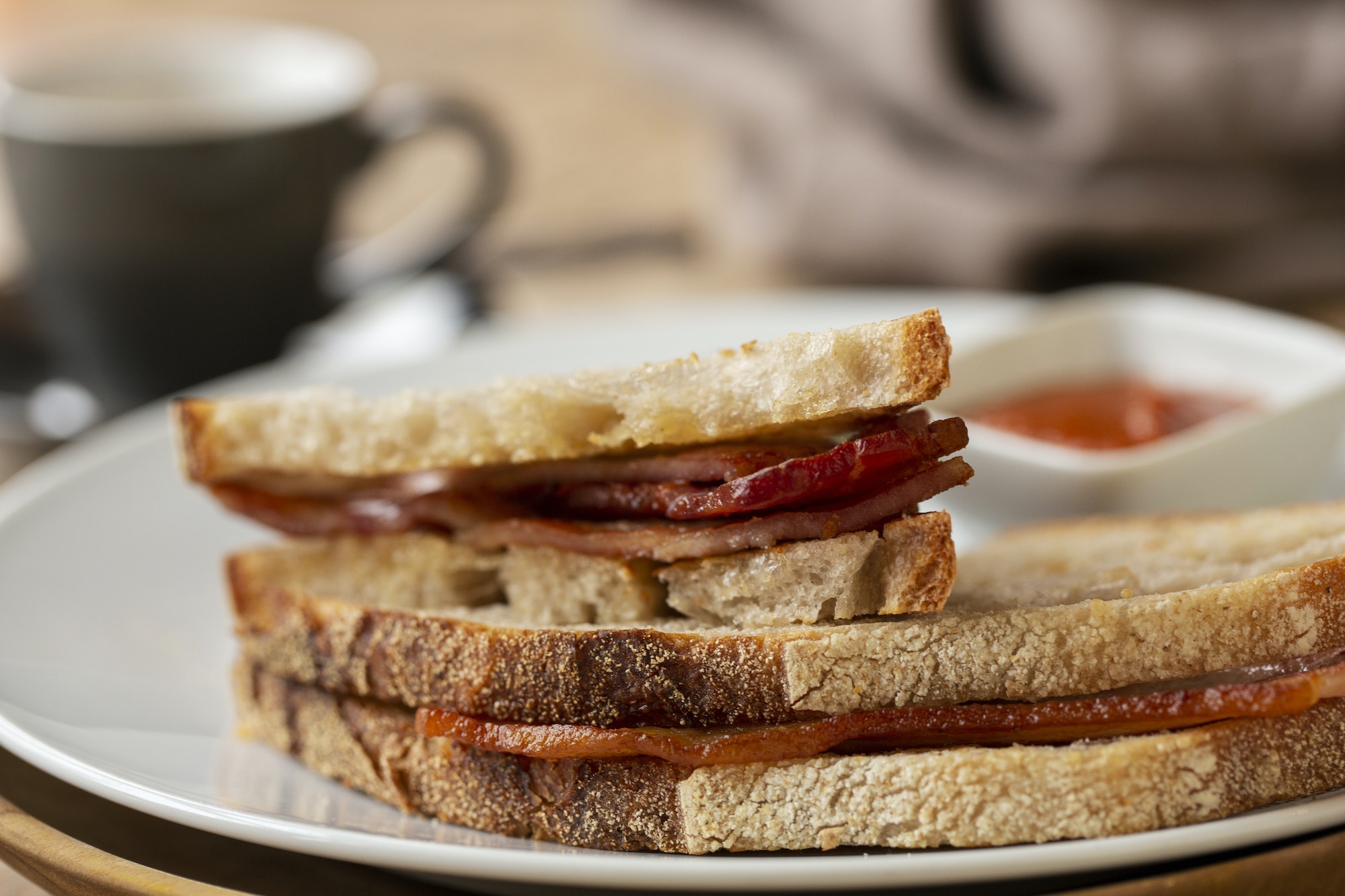 Close up of bacon sandwich and small bowl of home made tomato sauce in a cafe.